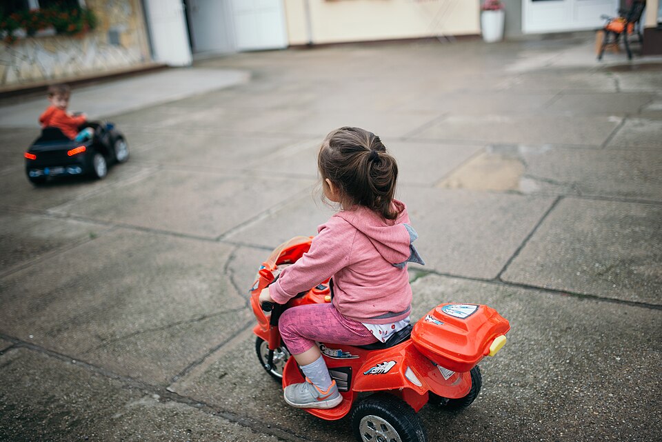 Zdjęcie ilustracyjne: A boy and a girl riding electric toy vehicles in the yard.jpg